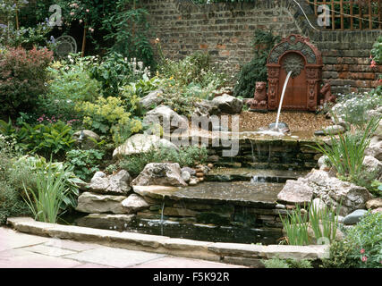 Lion fontana sulla parete sopra la cascata su gradini di pietra refilato con rocce in un paese walled garden in estate Foto Stock