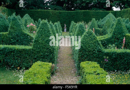 Un sentiero di ghiaia attraverso topiaria da arbusti agganciato nella piramidi in un paese grande giardino Foto Stock