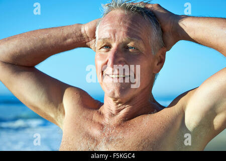 Testa e la spalla ritratto di una matura età uomo sorridente con vista oceano e le onde sullo sfondo Foto Stock