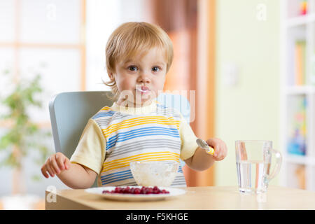 Carino bambino piccolo ragazzo mangiare con il cucchiaio nella nursery Foto Stock