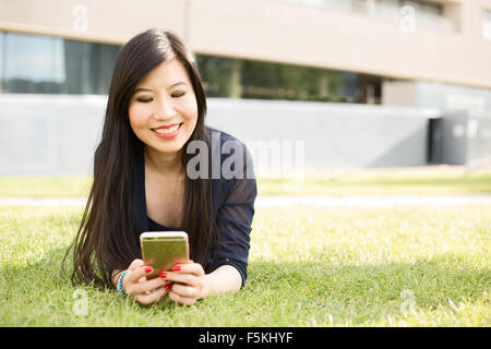 Ragazza giapponese giacente su erba inviando un messaggio di testo Foto Stock