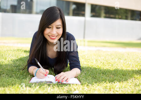 Giovane donna giapponese giacente sull'erba iscritto in un libro Foto Stock