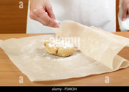 Un baker laminazione di un impasto tra due fogli di carta da forno. Fare pasta per torta ungherese. Serie. Foto Stock