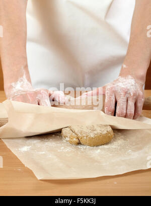 Un baker laminazione di un impasto tra due fogli di carta da forno. Fare pasta per torta ungherese. Serie. Foto Stock