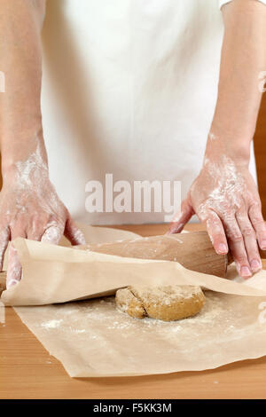 Un baker laminazione di un impasto tra due fogli di carta da forno. Fare pasta per torta ungherese. Serie. Foto Stock