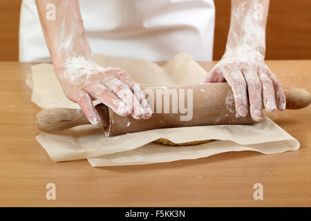 Un baker laminazione di un impasto tra due fogli di carta da forno. Fare pasta per torta ungherese. Serie. Foto Stock