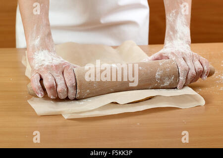 Un baker laminazione di un impasto tra due fogli di carta da forno. Fare pasta per torta ungherese. Serie. Foto Stock