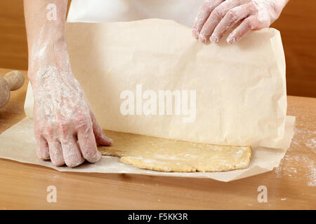 Un baker laminazione di un impasto tra due fogli di carta da forno. Fare pasta per torta ungherese. Serie. Foto Stock