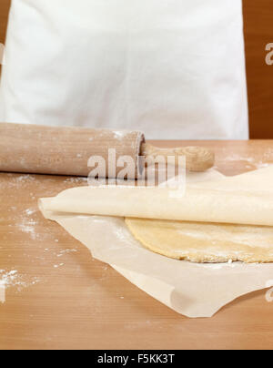 Un baker laminazione di un impasto tra due fogli di carta da forno. Fare pasta per torta ungherese. Serie. Foto Stock