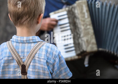 In stile vintage ragazzino con giarrettiere ascoltare attentamente un musicista di strada di suonare la fisarmonica / Infanzia concerto di musica Foto Stock