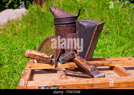 Vintage fumatore e diversi tipi di apicoltore coltelli, filtro di metallo, gabbia per ape regina sulla scatola di legno. Foto Stock