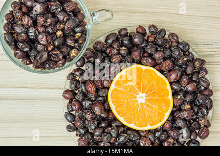 Essiccato cinorrodi e fette di arancia disposte in due ciotole sullo sfondo di legno. Uno stile di vita sano. Foto Stock