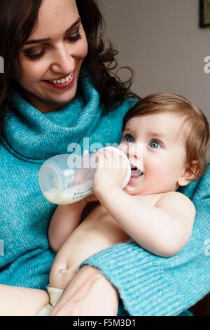 Madre guarda baby boy bere latte dalla bottiglia Foto Stock