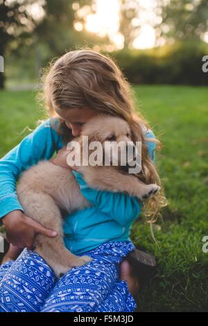 Ragazza abbracciando puppy in giardino al tramonto Foto Stock