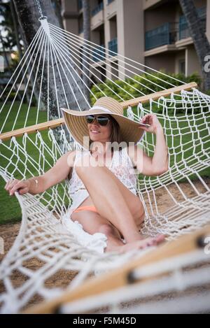 Metà donna adulta indossando cappello e reclinabili bikini in amaca, Maui, Hawaii, STATI UNITI D'AMERICA Foto Stock