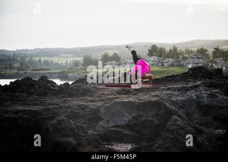 La donna a costa la pratica dello yoga in equilibrio su mani, punto Hawea, Maui, Hawaii, STATI UNITI D'AMERICA Foto Stock