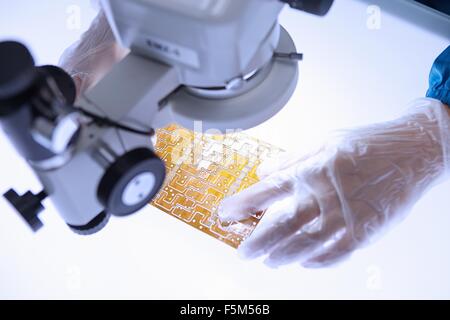 Mano del lavoratore di sesso femminile che usando microscopio per esaminare il circuito flessibile in elettronica flessibile fabbrica camera pulita Foto Stock
