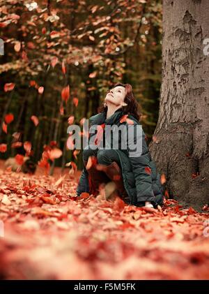 Donna gettando le foglie di autunno in aria nella foresta, Dyrehaven, Copenhagen, Danimarca Foto Stock