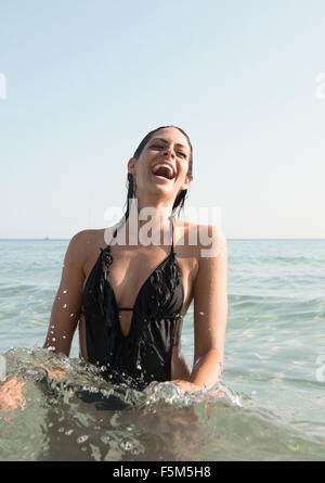 Ritratto di giovane donna che indossa il costume da bagno spruzzi in mare Foto Stock