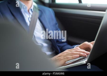 Giovane imprenditore in chat digitando su laptop nel sedile posteriore della macchina Foto Stock