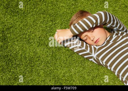 Angolo di Alta Vista del ragazzo che giace sull'erba faccia di schermatura occhi chiusi Foto Stock