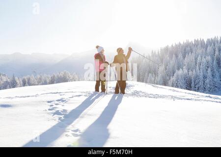 Coppia senior su paesaggi innevati holding walking guardando lontano, Sattelbergalm, Tirolo, Austria Foto Stock