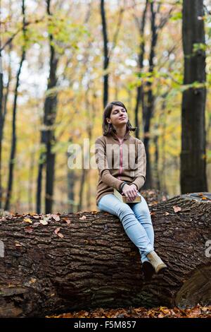 Ragazza fantasticando sul tronco di albero nella foresta di autunno Foto Stock