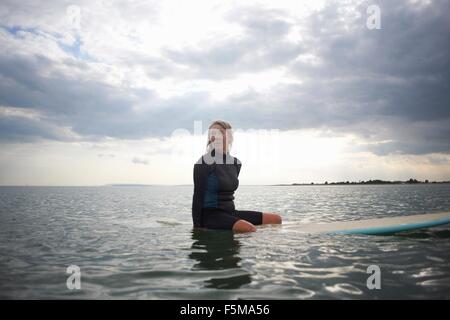 Senior donna seduta sulla tavola da surf in mare Foto Stock