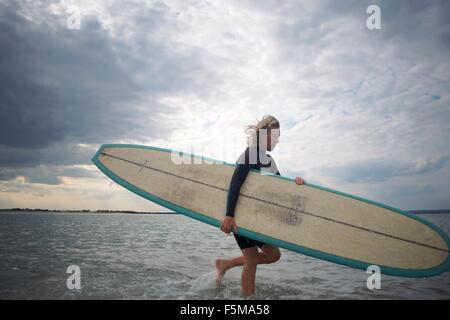 Senior donna a piedi dal mare, portando le tavole da surf Foto Stock