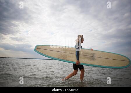 Senior donna a piedi dal mare, portando le tavole da surf Foto Stock