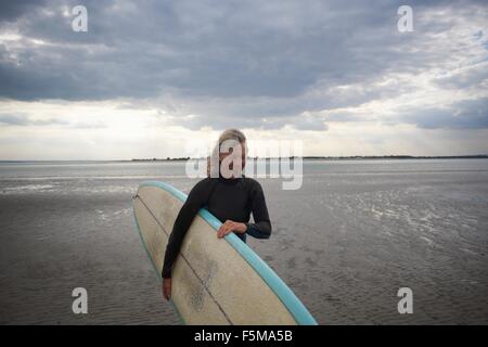 Senior donna a piedi dal mare, portando le tavole da surf Foto Stock