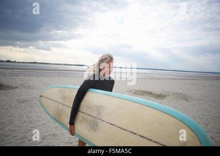 Senior donna a piedi dal mare, portando le tavole da surf Foto Stock