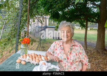 Senior che pongono la donna accanto al vassoio di uova in agriturismo Foto Stock