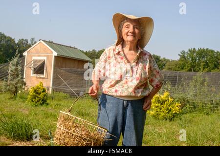 Senior donna cestello di trasporto della paglia in agriturismo Foto Stock