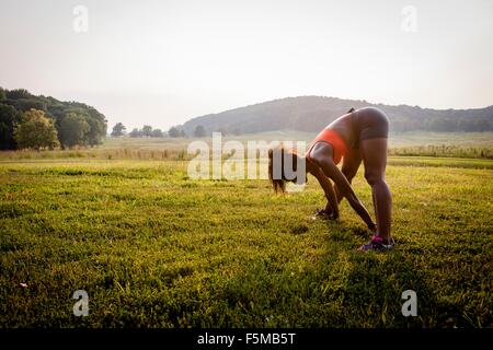 Giovani femmine runner toccando le dita dei piedi nel parco rurale Foto Stock