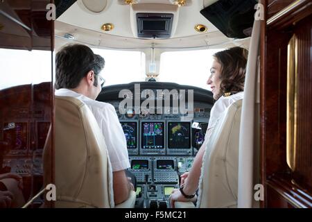 Vista posteriore del maschio e femmina piloti parlano in cabina di pilotaggio di un jet privato Foto Stock