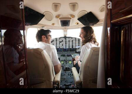 Vista posteriore del maschio e femmina chat pilota nel cockpit di jet privato Foto Stock