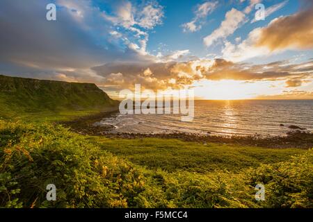 Sun impostazione sull orizzonte oltre oceano, Giants Causeway, Bushmills, County Antrim, Irlanda, Regno Unito Foto Stock