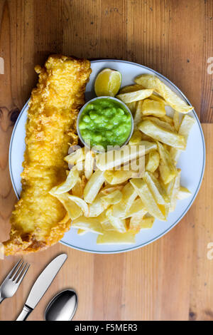 Inglese Cod pesce e patatine con fiacco piselli in una piastra su un tavolo Foto Stock