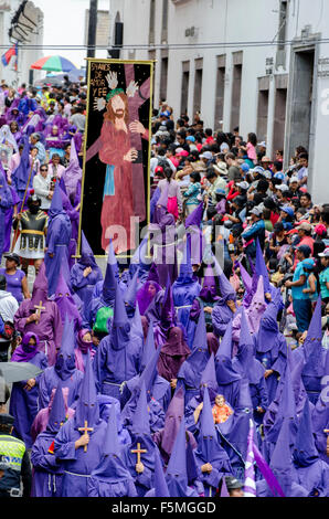 Cucuruchos accompagnare un banner che mostra Gesù porta la croce durante la processione del Venerdì Santo a Quito, Ecuador. Foto Stock