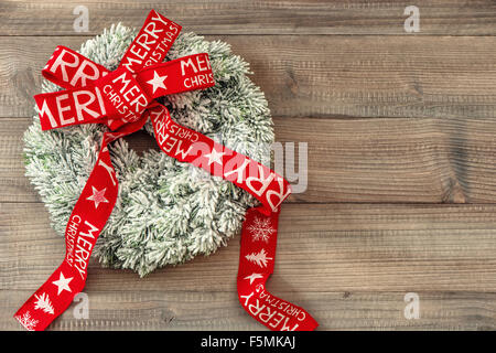 Ghirlanda di Natale con nastro rosso su sfondo di legno. Decorazione di festa. Auguri di Buon Natale Foto Stock