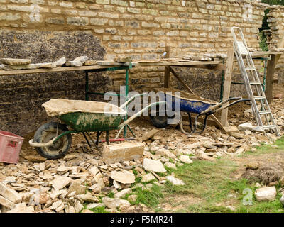 Vecchio naturale, giardino di pietra calcarea parete riparazioni e ristrutturazioni con builder strumenti, carriole, tralicci, ponteggi e tavole. Foto Stock