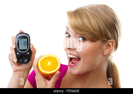 Donna felice azienda glucometro con risultato positivo di misura di livello di zucchero e mangiare fresche e mature, arancione Foto Stock