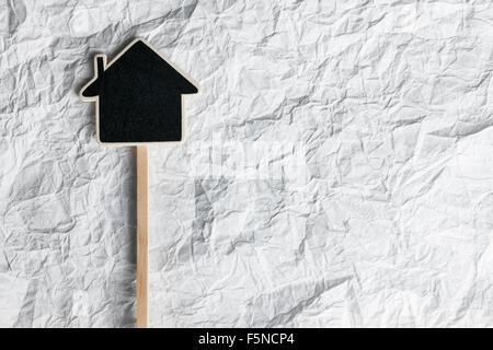 Puntatore di legno a forma di casa giacenti su una carta sgualcita, come sfondo Foto Stock