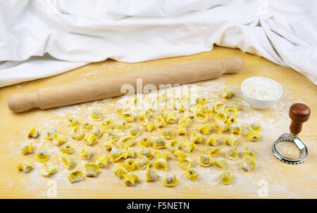 I tortellini emiliani casalingo italiano materie paste alimentari farcite con carne di manzo e di maiale, carne mattarello, la farina in una tazza e su una tavola di legno indietro Foto Stock