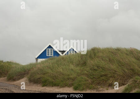 Una casa sulla spiaggia si accoccola dietro una duna di sabbia coperte in un mare di dune di erba. Questo darà la casa protezione dalle tempeste. Foto Stock