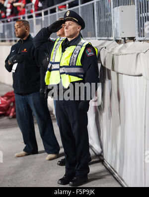 Columbus, Ohio, Stati Uniti d'America. 7 Nov, 2015. Un funzionario di polizia saluta la bandiera durante l inno nazionale a una stagione regolare il gioco tra la Ohio State Buckeyes e del Minnesota Golden i Gopher in Columbus, Ohio. Brent Clark/CSM/Alamy Live News Foto Stock