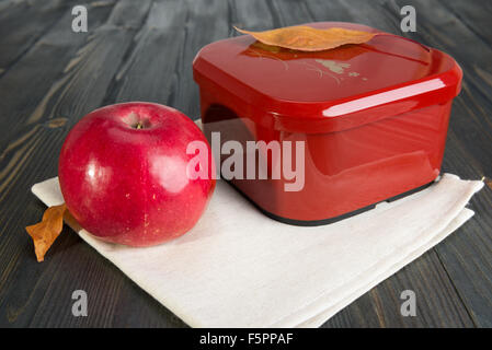 Red apple e una scatola chiusa per la scuola prima colazione sul buio superficie in legno Foto Stock