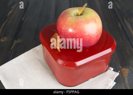 Red apple e una scatola chiusa per la scuola prima colazione sul buio superficie in legno Foto Stock