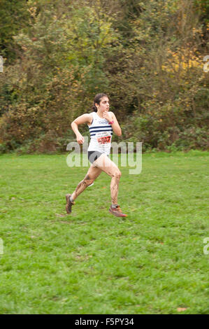 Bruna giovane lady runner rivestito in pioggia e fango affacciate agli elementi nel cross country race con silenziatore campo di erba al calpestio Foto Stock